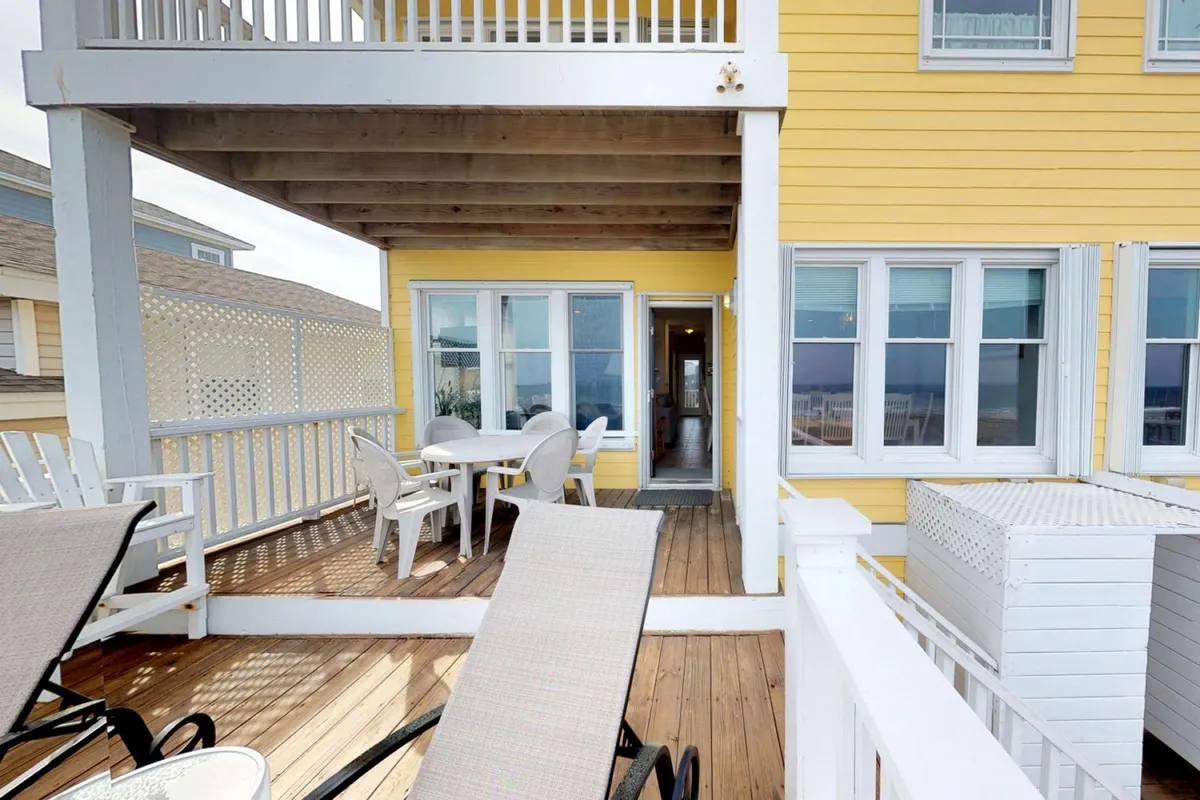 An inviting oceanfront deck with yellow exterior walls, outdoor dining table, chairs, and deck loungers—all overlooking the wide expanse of the Atlantic. The setting is ideal for al fresco meals, morning coffee, or relaxing to the sound of the waves.