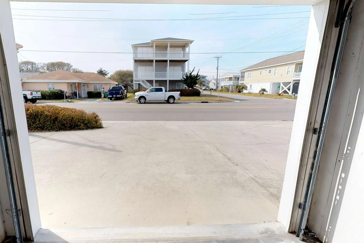 A view of the exterior parking area with a visible garage opening, street view, and neighboring houses. The driveway appears spacious and accessible.