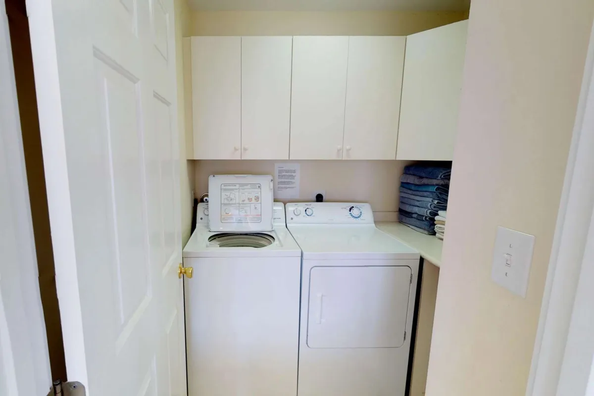A bright, functional laundry area featuring a washing machine, dryer, and overhead storage cabinets. The space appears organized and clean, emphasizing convenience and practicality for guests.