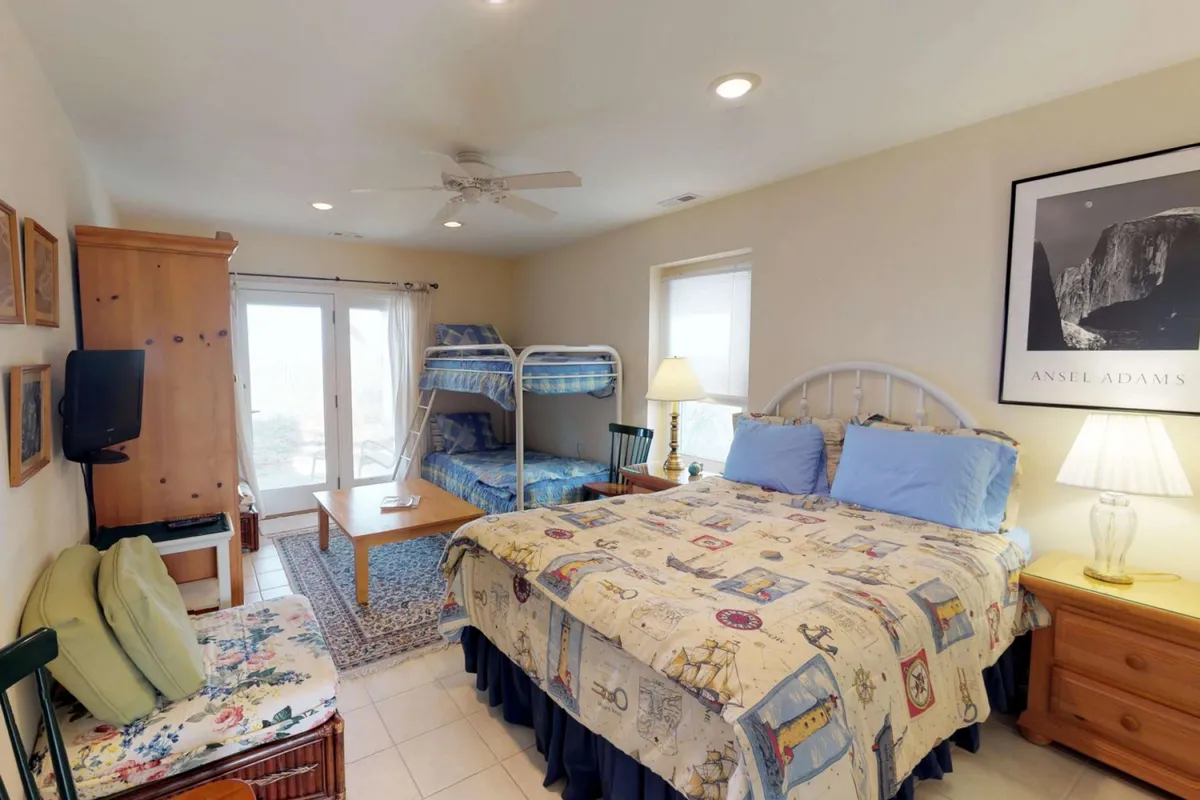 A bright and inviting family-friendly bedroom with a queen bed featuring patterned bedding and a bunk bed, perfect for children. A wooden dresser, bedside lamp, and cheerful wall art create a warm, welcoming atmosphere for guests of all ages.