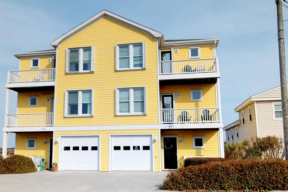 The exterior of a bright yellow townhome with balconies and garage doors, set against a clear sky. The balconies suggest spaces for relaxing after adventures, and the home's location hints at proximity to local attractions.