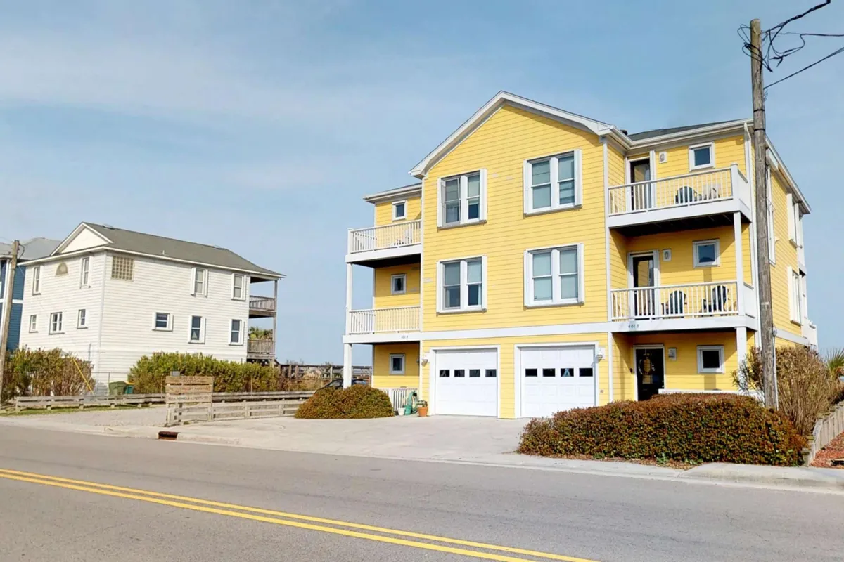 The image showcases the bright yellow exterior of Bramhall by the Sea, featuring inviting balconies and a well-landscaped yard. The presence of outdoor seating and balconies suggests spaces ideal for social gatherings, barbecues, or enjoying drinks at sunset—perfect for guests eager to make the most of group activities and al fresco dining.
