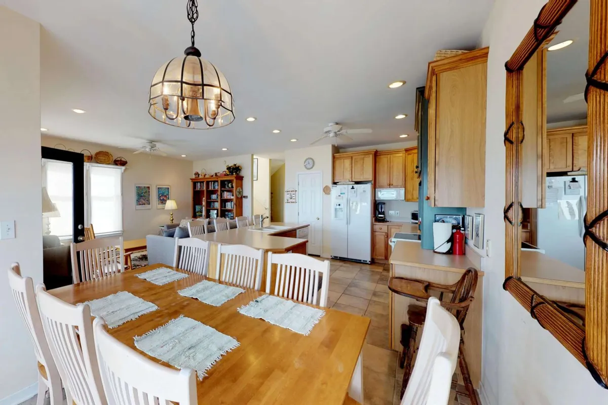 A formal dining area featuring a large table set for eight, illuminated by a chandelier, with the adjoining kitchen in view. The room is styled for celebratory meals, game nights, and memorable family gatherings, embodying a warm, festive spirit.
