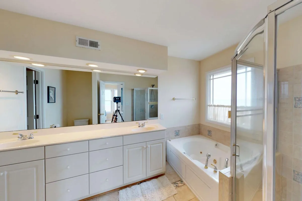 A stylish ensuite bathroom with a double vanity, a soaking bathtub, a spacious shower enclosure, and a large mirror. The design is airy and bright, evoking a spa-like sense of relaxation and luxury.